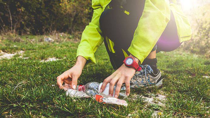 persona che pratica il plogging e raccoglie i rifiuti che sono su un prato